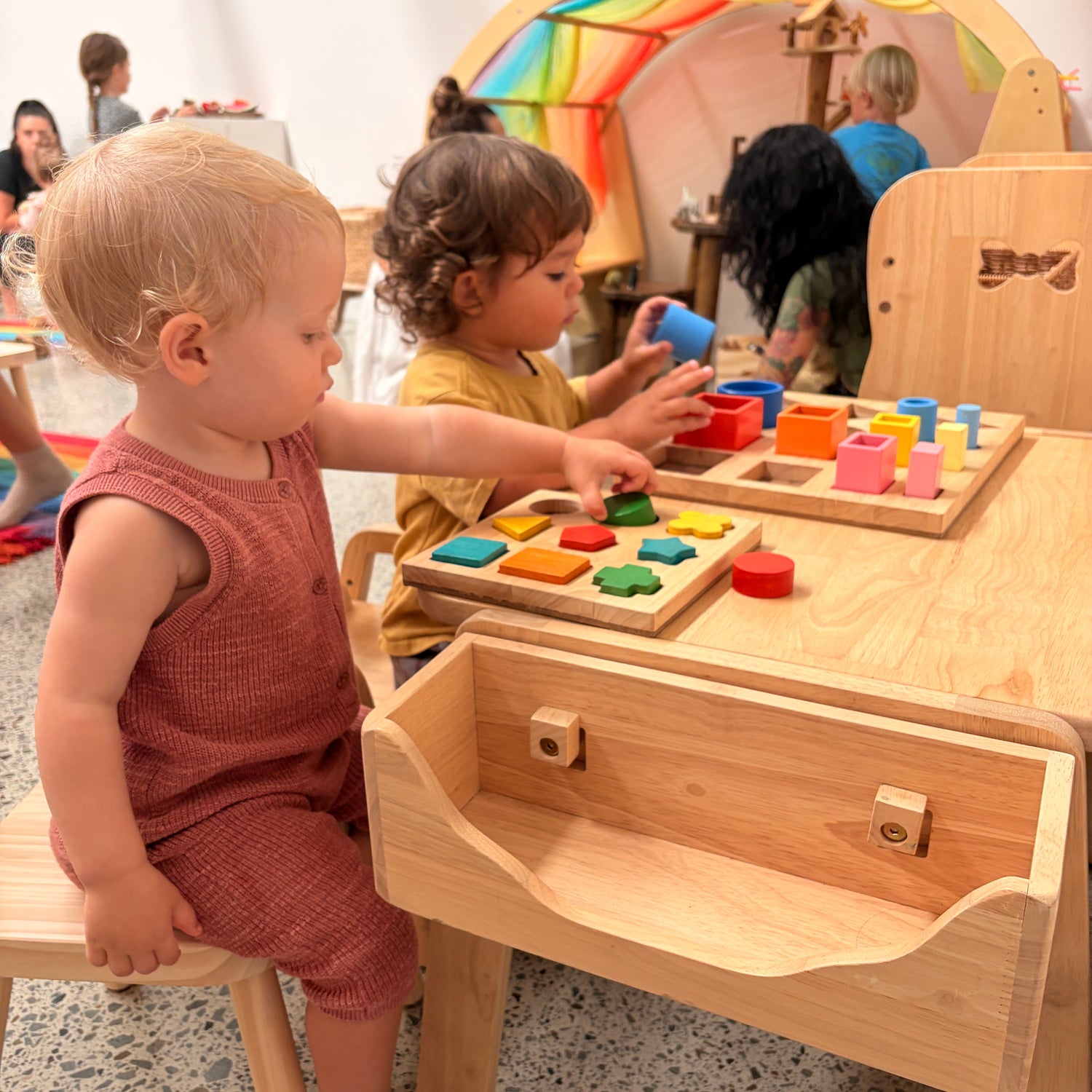Two children playing with colorful wooden toys at a wooden table.